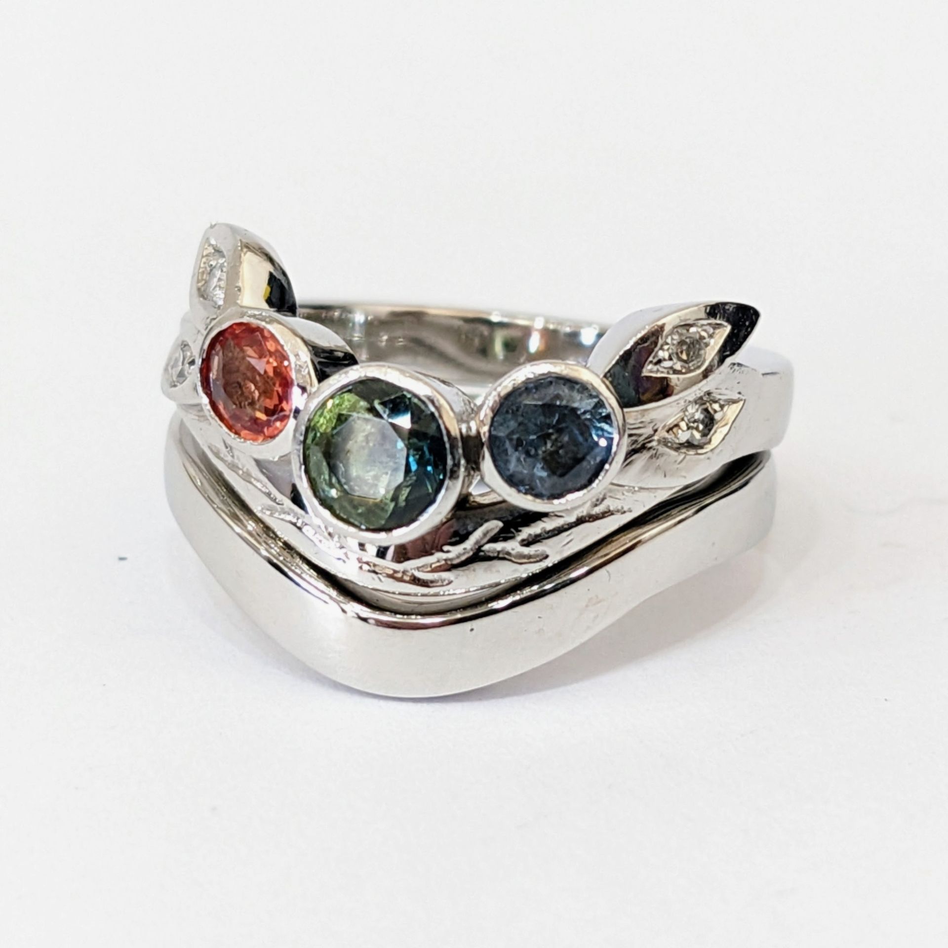 Ring set with orange, green and blue gemstones and leaf details, with a shaped band