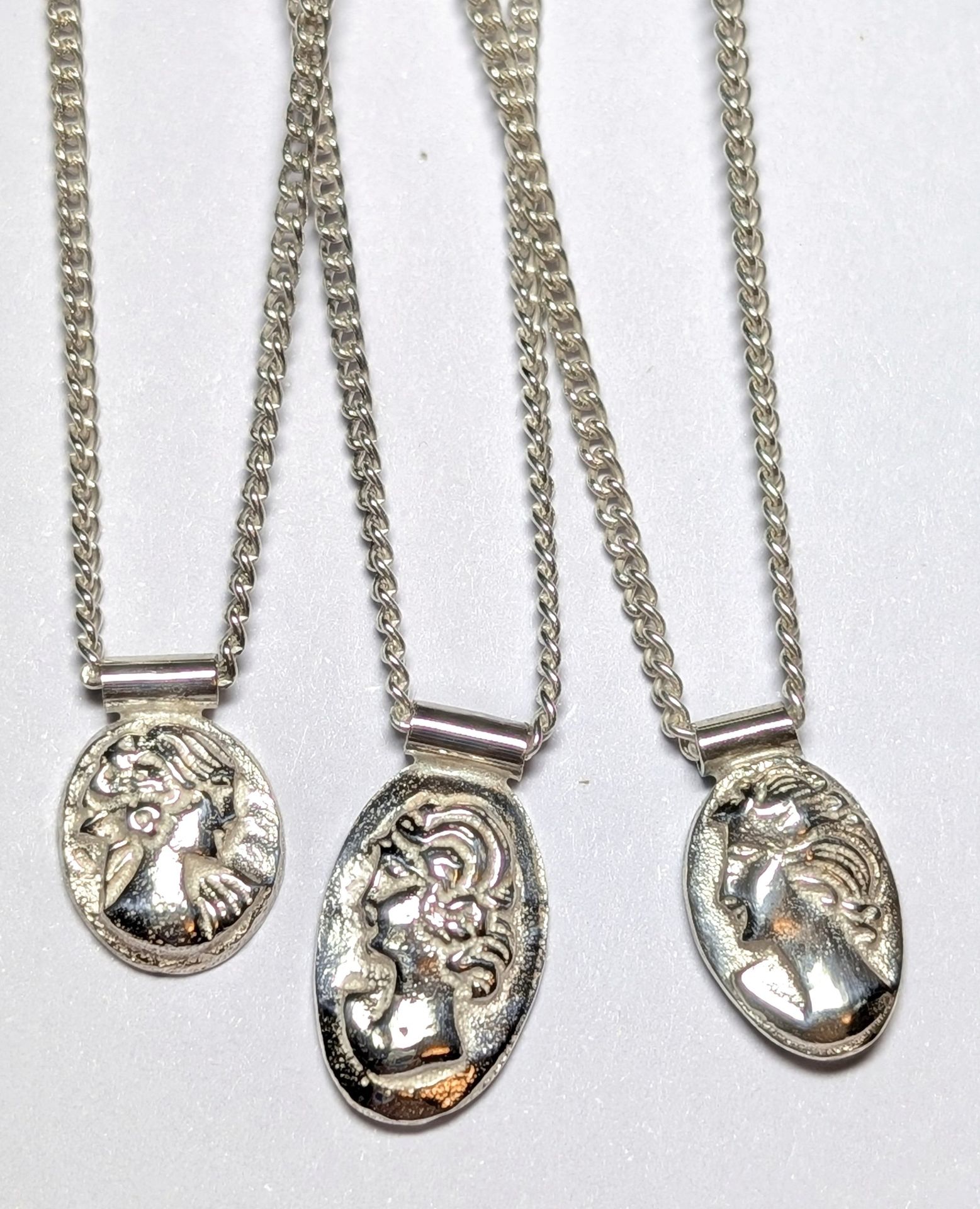 Three silver cameo-inspired pendants on chains