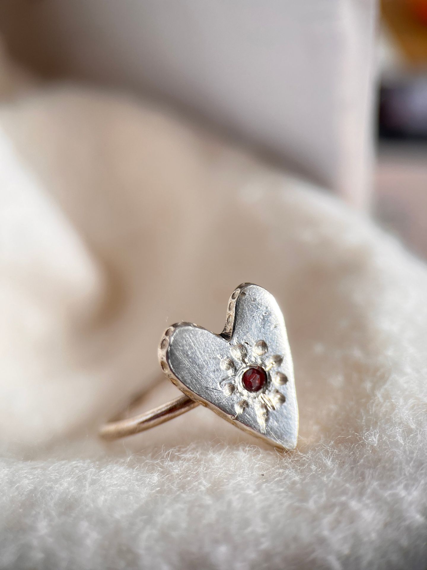 Silver heart ring with a small red stone in a starburst setting