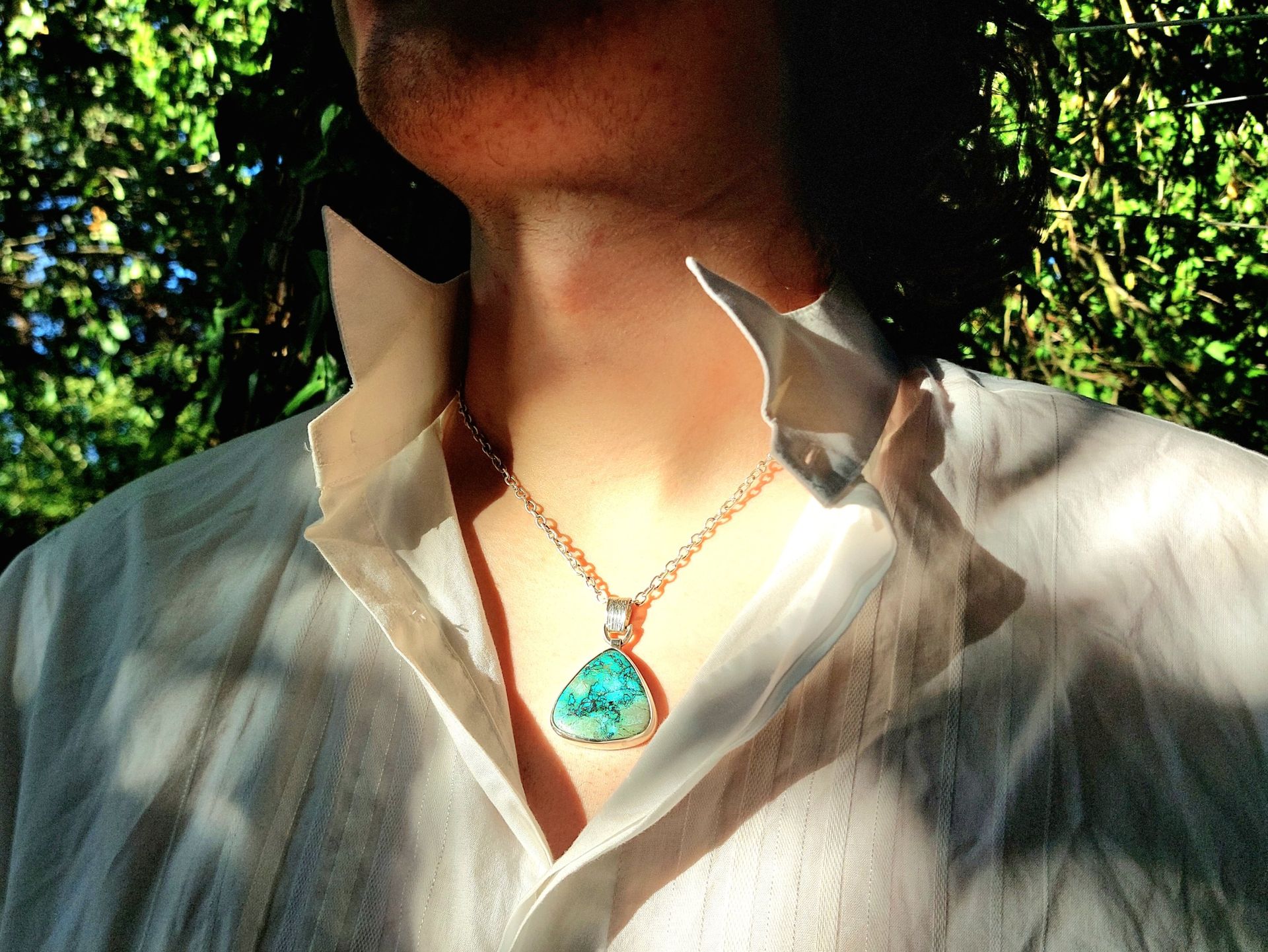 Large blue-green stone pendant in a silver setting, worn with an open white shirt