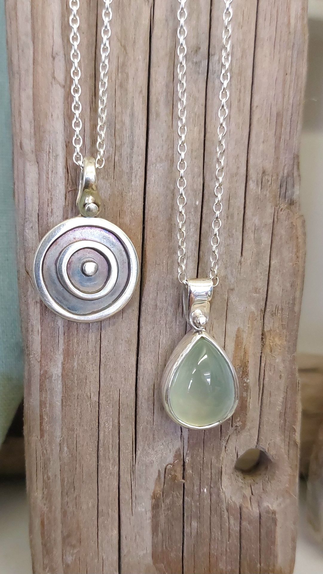 Silver spiral disc pendant and pale green stone drop pendant hanging on driftwood