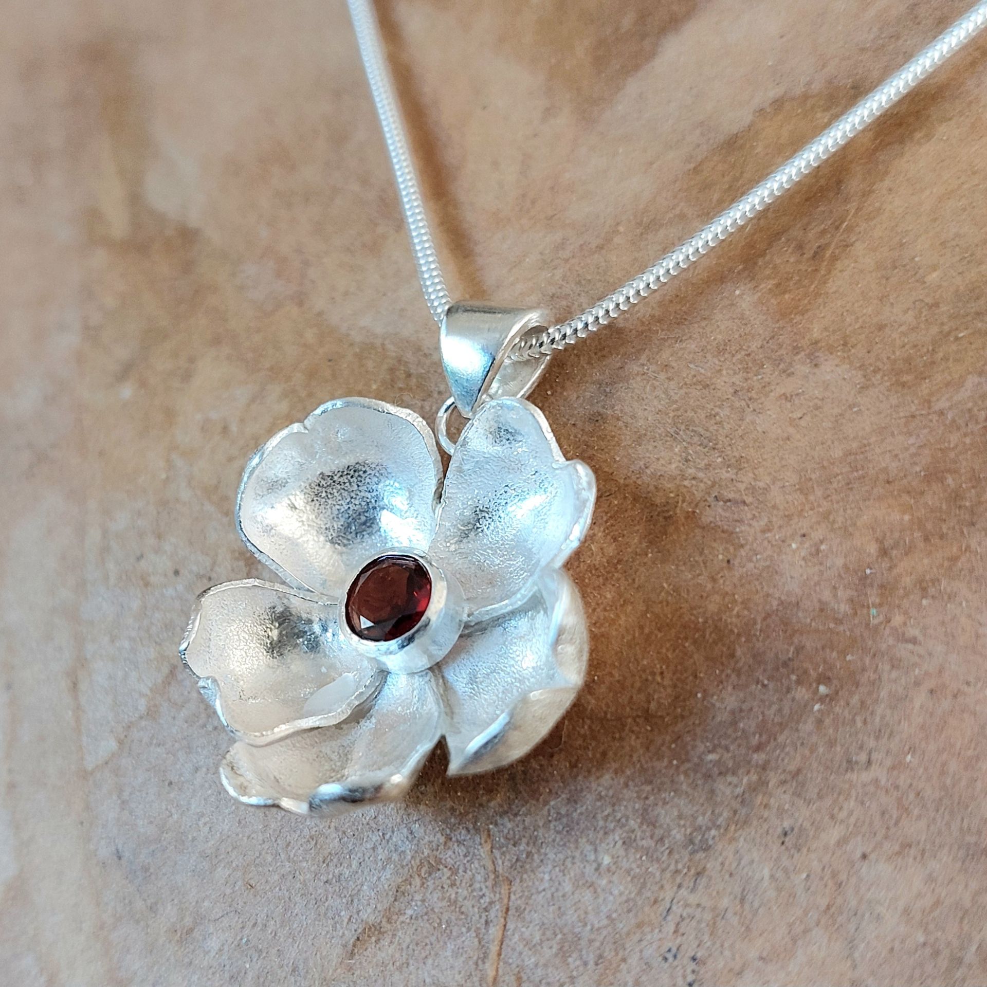 Textured silver flower pendant with a red stone centre